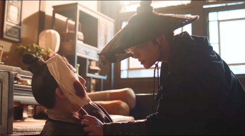 Scene from modern Chinese drama The Road To Splendor Episode 14 recap of a man with a straw hat aiming a crossbow at an injured man with a bandage around his head