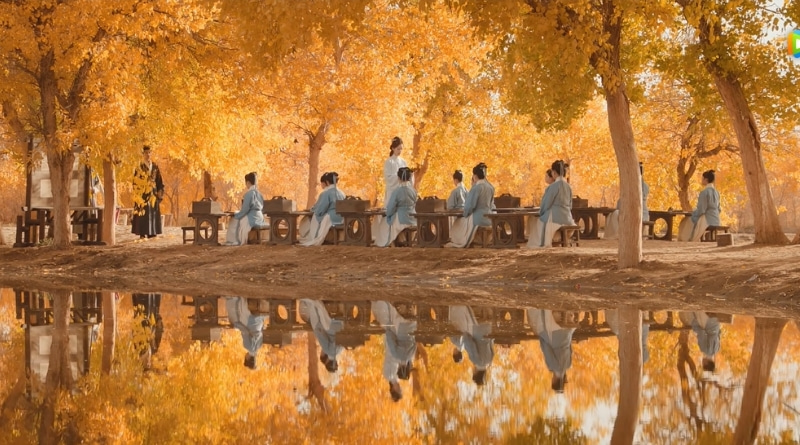 Scene from modern Chinese drama The Road To Splendor Episode 16 recap of a teacher teaching a classroom of women by the lake under the autumn yellow trees