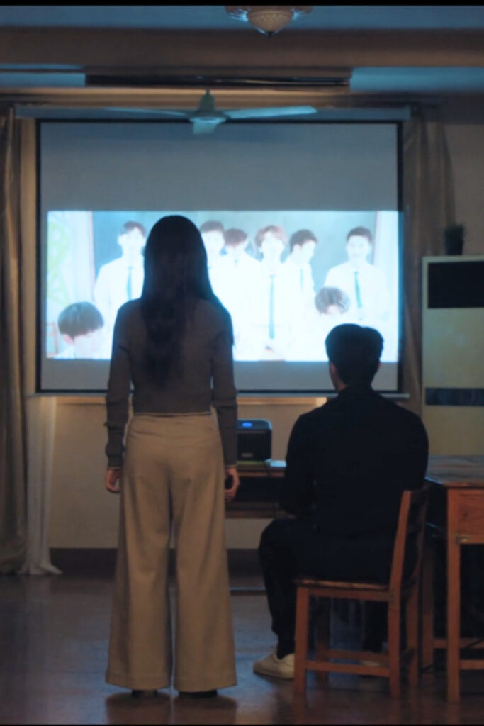 Scene from modern Chinese drama Road To Success Episodes 15-16 recap of a man and a woman watching a video of a bunch of high school boys, on the screen