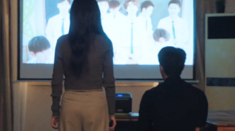 Scene from modern Chinese drama Road To Success Episodes 15-16 recap of a man and a woman watching a video of a bunch of high school boys, on the screen