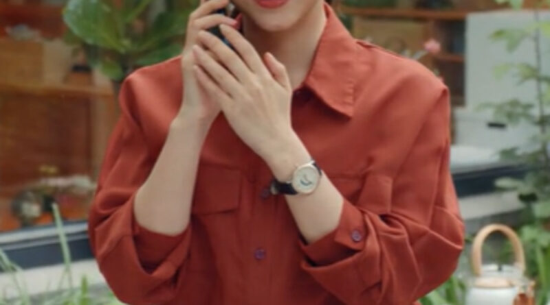 Scene from modern Chinese drama Road Home Episode 26 recap and review of a woman on her phone and she is smiling wearing red shirt and black skirt