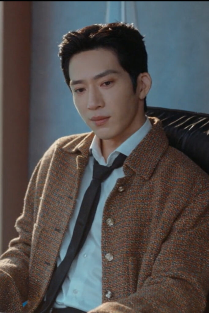 Scene from modern Chinese drama The Early Spring Episode 6 recap and review of a man sitting in his office chair, thinking, wearing a brown jacket and black tie